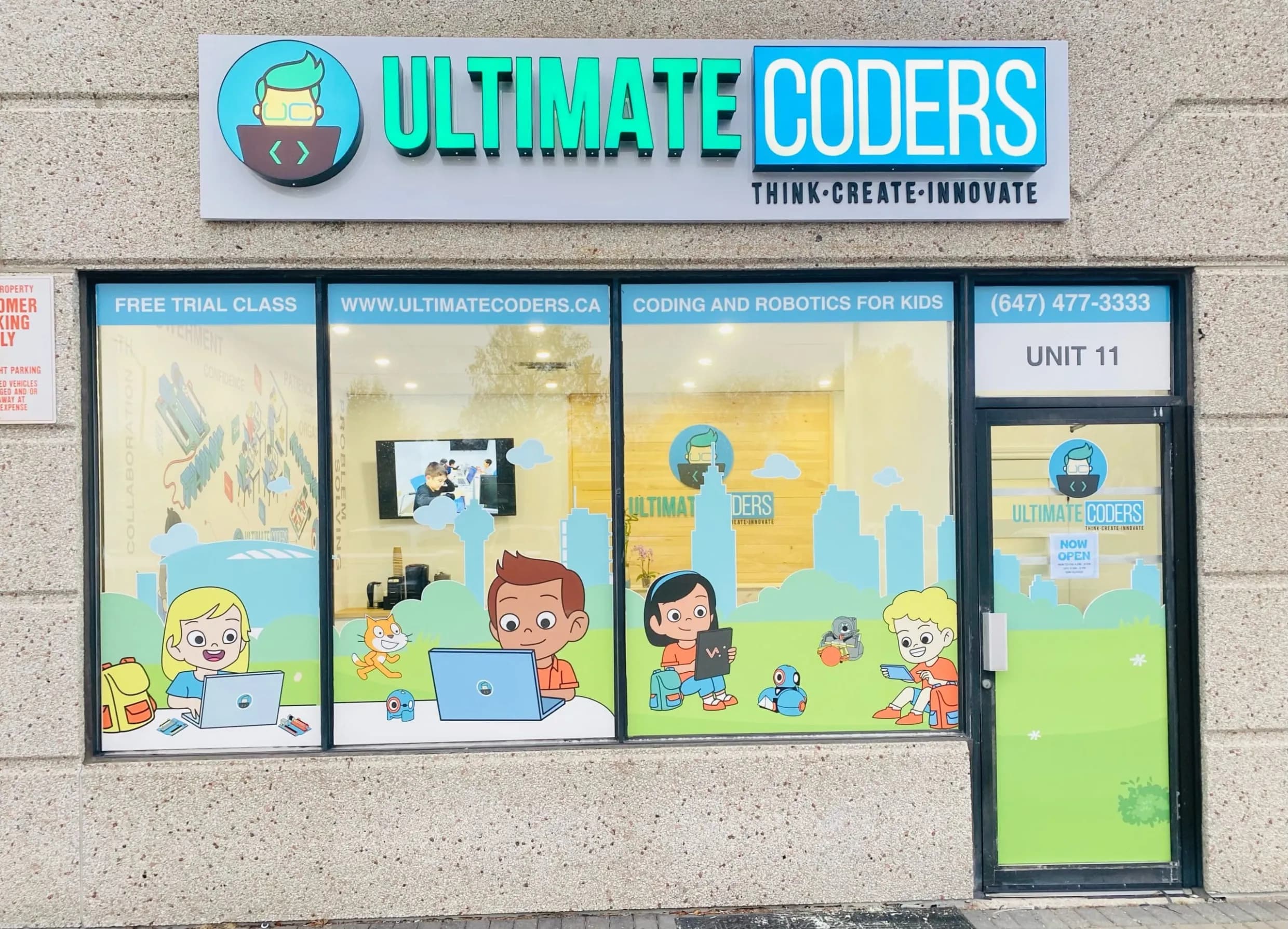 The exterior of an Ultimate Coders centre: illuminated signage above a glass storefront, its windows painted with children at laptops and robots